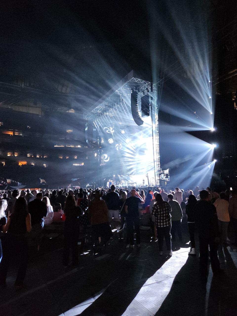 White stage light beams cutting through darkness over a standing crowd at Mercedes-Benz Stadium