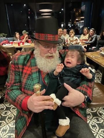 Stage Christmas Party — Jeffry holding the wailing toddler and his cane, the party going on behind them, Sun · Dec 17, 2023