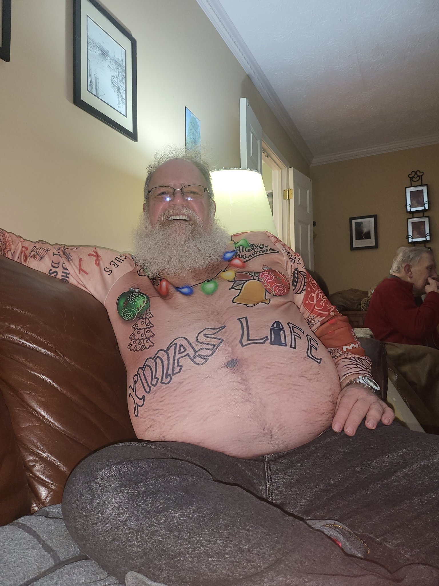 Stage Christmas Party — Jeffry at home in his “XMAS LIFE” Christmas shirt, laughing on the couch — from the Christmas collection