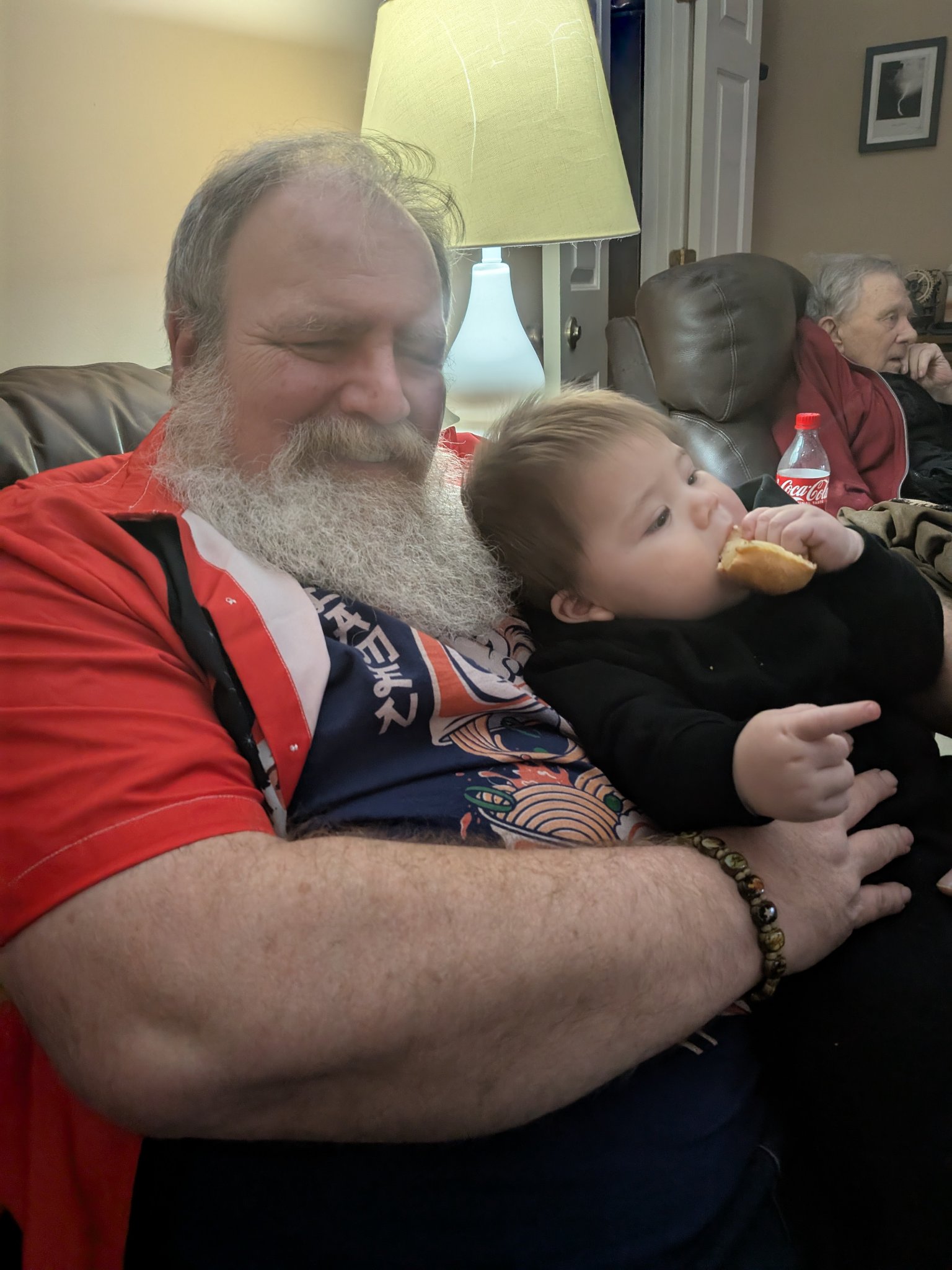 A visit with the grandkids — Jeffry on the couch holding the toddler, who is gnawing a piece of bread, Sat · Dec 21, 2024